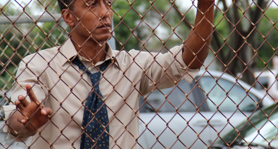 Byrd (Andre Royo) standing by the fence of the basketball court.